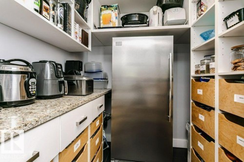 Stainless steel refrigerator integrated within a pantry featuring white cabinetry, granite-finish countertops, open shelving, and wooden pull-out drawers - 9035 Saskatchewan Drive, Edmonton, AB 