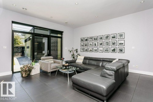 Spacious living area featuring large format tile flooring, recessed lighting, expansive glass sliding doors, and a high ceiling - 9035 Saskatchewan Drive, Edmonton, AB 