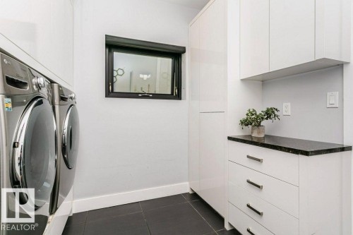 Laundry area featuring a dark framed window, white baseboards, dark flooring, and white cabinetry with a dark countertop - 9035 Saskatchewan Drive, Edmonton, AB 