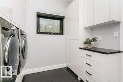 Laundry area featuring a dark framed window, white baseboards, dark flooring, and white cabinetry with a dark countertop - 