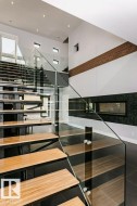 Modern floating staircase featuring wood-finish treads and clear glass railings - 