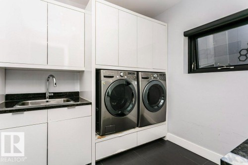 Laundry area featuring stacked appliances, built-in cabinetry, and a utility sink with a dark stone-finish countertop - 9035 Saskatchewan Drive, Edmonton, AB 