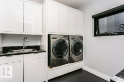 Laundry area featuring stacked appliances, built-in cabinetry, and a utility sink with a dark stone-finish countertop - 