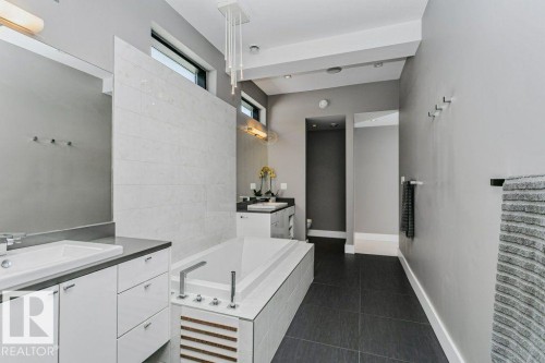 Contemporary bathroom featuring a built-in soaking tub, dual floating vanities with integrated sinks, dark tile flooring, and transom windows - 9035 Saskatchewan Drive, Edmonton, AB 