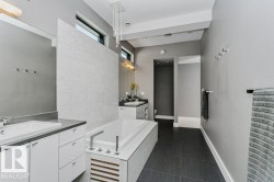 Contemporary bathroom featuring a built-in soaking tub, dual floating vanities with integrated sinks, dark tile flooring, and transom windows - 
