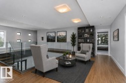 Open upper-level area featuring a glass railing system, wood-finish flooring, built-in shelving, recessed lighting, and multiple windows - 