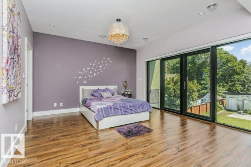 Spacious room featuring wood-finish flooring, a contemporary chandelier, recessed lighting, and a large sliding glass door opening to the exterior - 9035 Saskatchewan Drive, Edmonton, AB 