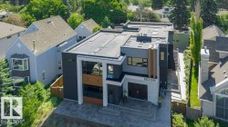 Contemporary architectural design featuring a flat roofline, dark grey and white exterior finishes, large rectangular windows, a stone-clad entrance, and a paved driveway - 