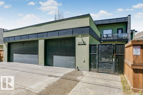 Contemporary exterior featuring a two-car garage, a second-story balcony with glass railing, and a wrought iron entry gate - 9035 Saskatchewan Drive, Edmonton, AB 