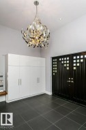 Entryway featuring a modern chandelier, dark wood-finish double doors with grid-patterned windows, built-in white cabinetry, recessed lighting, and large format dark tile flooring - 