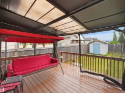 Covered wood-finish deck featuring a translucent roof, a wood privacy fence, and a storage shed with a light blue door - 