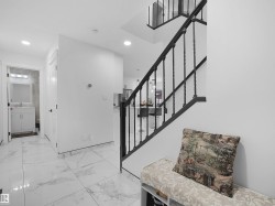 Foyer featuring large format tile flooring, black iron stair railing, recessed lighting, and a white vanity with a rectangular mirror and wall-mounted light fixture in the adjacent space - 