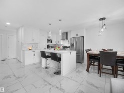 Modern kitchen featuring white cabinetry, a central island with pendant lighting, stainless steel appliances, and large format marble-look floor tiles - 