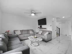 Living area featuring large format white tile flooring with gray veining, white walls, and a ceiling fan with integrated lighting - 