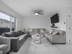 Spacious living area featuring large format white tile flooring, a contemporary ceiling fan with integrated lighting, and a built-in wall shelf - 