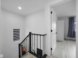 Hardwood-finish flooring extending from the hallway into an adjacent room, complemented by a white paneled door with matte black hardware - 