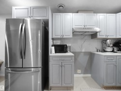 Kitchen featuring upper white cabinetry, lower gray cabinetry, stainless steel appliances, and a marble-patterned backsplash - 