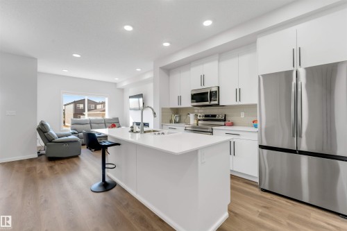 Modern kitchen featuring white cabinetry, stainless steel appliances, a center island with countertop seating, and wood-finish flooring throughout - 788 Mattson Drive, Edmonton, AB 