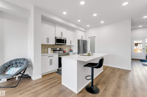 Modern kitchen featuring white cabinetry, stainless steel appliances, a white island with an undermount sink, and wood-finish flooring - 788 Mattson Drive, Edmonton, AB 