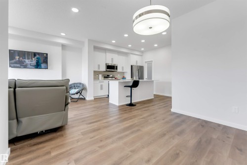 Open-concept living space featuring wood-finish flooring, recessed lighting, a modern drum pendant light, and a kitchen island with seating - 788 Mattson Drive, Edmonton, AB 