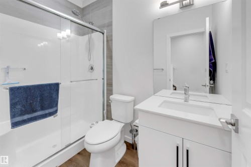 Bathroom featuring a tub/shower combination with sliding glass doors, a single vanity with an integrated sink and white countertop, and wood-finish flooring - 788 Mattson Drive, Edmonton, AB 