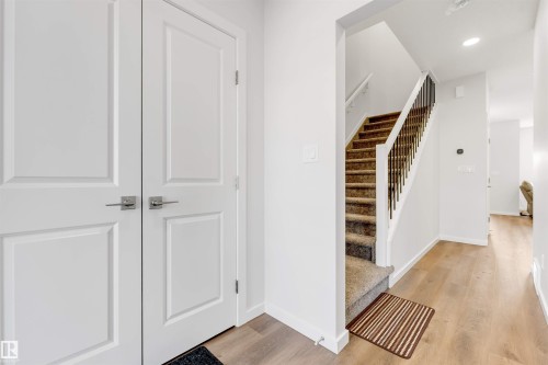 Entryway featuring wood-finish flooring, white panel doors with brushed nickel hardware, and a staircase with carpeted treads and wrought iron spindles - 788 Mattson Drive, Edmonton, AB 