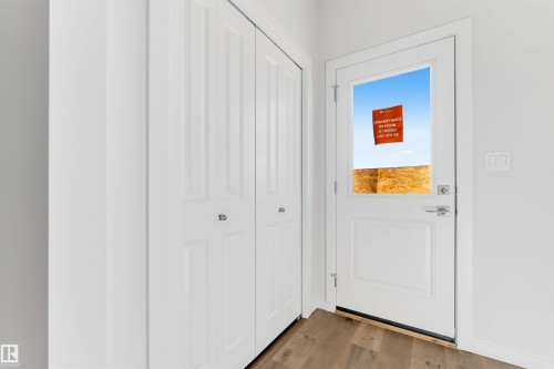 Entryway featuring a white paneled door with an upper glass insert, wood-finish flooring, and white bifold closet doors - 788 Mattson Drive, Edmonton, AB 