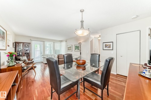 Open-concept dining area featuring wood-finish flooring, a contemporary chandelier, and a glass-top dining table - 7930 111 Street, Edmonton, AB - Indoor Photo Showing Dining Room
