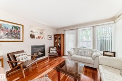 Living area featuring wood-finish flooring, a built-in fireplace, recessed shelving with glass accents, and large windows with vertical blinds - 