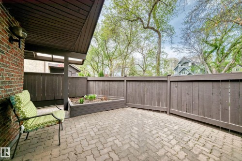 Private patio, accessed from living room.  Paved patio featuring a raised garden bed, brown privacy fencing, and a brick exterior wall with an attached outdoor light fixture - 7930 111 Street, Edmonton, AB - Outdoor With Deck Patio Veranda With Exterior