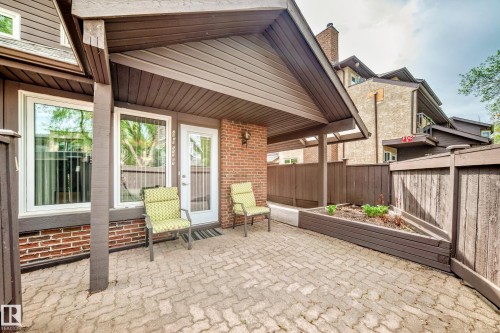 Covered outdoor patio area featuring brick-patterned pavers and a wood-slat privacy fence - 7930 111 Street, Edmonton, AB - Outdoor With Deck Patio Veranda With Exterior