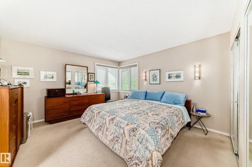 Spacious bedroom featuring light neutral wall tones, plush carpeting, corner windows with horizontal blinds, built-in wall sconces, and mirrored closet doors.  Access door to extra ATTIC STORAGE space for luggage, etc. - 7930 111 Street, Edmonton, AB - Indoor Photo Showing Bedroom
