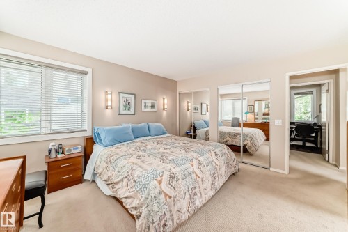 Carpeted bedroom featuring a large window with blinds, wall sconces, and mirrored closet doors - 7930 111 Street, Edmonton, AB - Indoor Photo Showing Bedroom
