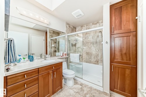 Bathroom featuring a vanity with a rectangular sink, a shower-tub combination with a sliding glass door, extensive wall and floor tiling, and built-in cabinetry - 7930 111 Street, Edmonton, AB - Indoor Photo Showing Bathroom