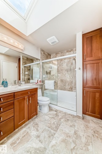 Bathroom with a skylight, a wood-finish vanity with a light-colored countertop, and a shower-over-tub combination with a glass enclosure - 7930 111 Street, Edmonton, AB - Indoor Photo Showing Bathroom
