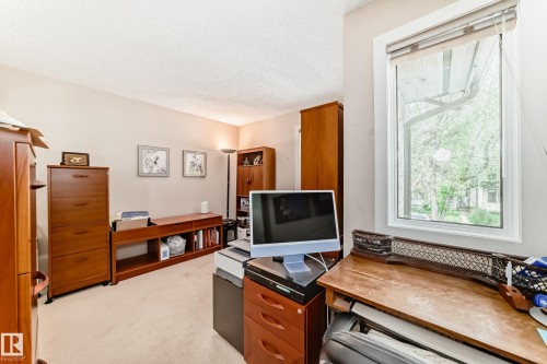 Carpeted room featuring a large window with white trim, a textured ceiling, and light-colored walls - 7930 111 Street, Edmonton, AB - Indoor