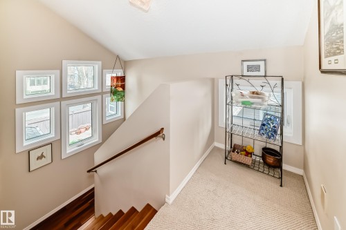 Split-level landing featuring a collection of six distinct windows, a wooden handrail, and wood-finish flooring transitioning to carpeted upper level - 7930 111 Street, Edmonton, AB - Indoor Photo Showing Other Room