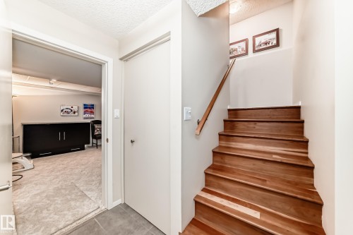 Hardwood staircase with natural wood handrail, light wall paint, and textured ceiling - 7930 111 Street, Edmonton, AB - Indoor Photo Showing Other Room