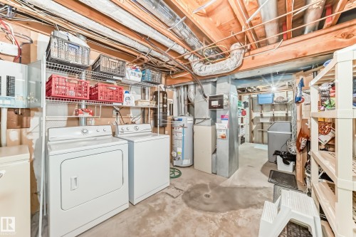 Basement utility area featuring a washer and dryer, exposed ceiling joists, ductwork, and a water heater.  WATER SOFTENER INCLUDED. - 7930 111 Street, Edmonton, AB - Indoor Photo Showing Laundry Room