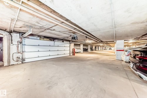 Underground parking garage featuring a white sectional garage door, concrete flooring, and exposed ceiling utilities - 7930 111 Street, Edmonton, AB - Indoor Photo Showing Garage