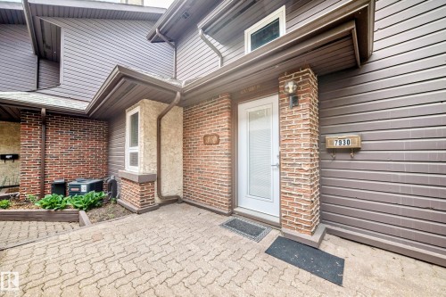 Brick and siding exterior featuring a white paneled entry door, an exterior wall sconce, and a paved walkway - 7930 111 Street, Edmonton, AB - Outdoor With Exterior