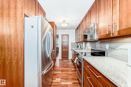 Galley kitchen featuring American Cherrywood flooring, stainless steel appliances, abundant cabinetry, stone-finish countertops, and a tiled backsplash - 7930 111 Street, Edmonton, AB - Indoor Photo Showing Kitchen With Upgraded Kitchen