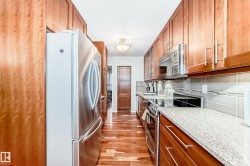 Galley kitchen featuring American Cherrywood flooring, stainless steel appliances, abundant cabinetry, stone-finish countertops, and a tiled backsplash - 