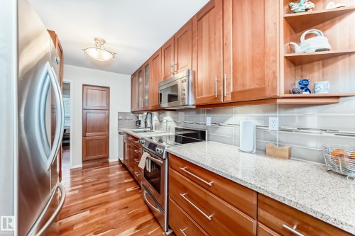 Kitchen featuring American Cherrywood flooring, stainless steel appliances, light-toned cabinetry, light-colored countertops, and a tiled backsplash - 7930 111 Street, Edmonton, AB - Indoor Photo Showing Kitchen
