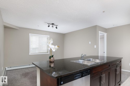 Kitchen island featuring a double basin sink, dark countertop, and integrated stainless steel dishwasher - 102 25 Element Dr, St. Albert, AB 