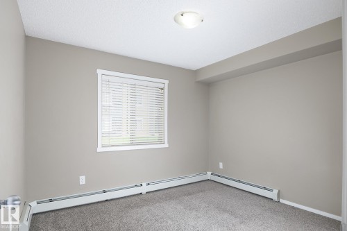 Carpeted room with neutral wall paint and a single window featuring horizontal blinds - 102 25 Element Dr, St. Albert, AB 