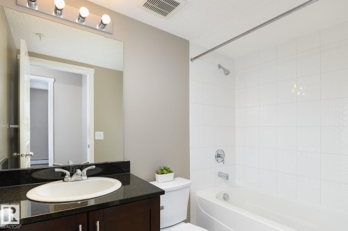 Bathroom featuring a dark wood-finish vanity with an undermount sink, dark countertop, and large wall-mounted mirror - 102 25 Element Dr, St. Albert, AB 