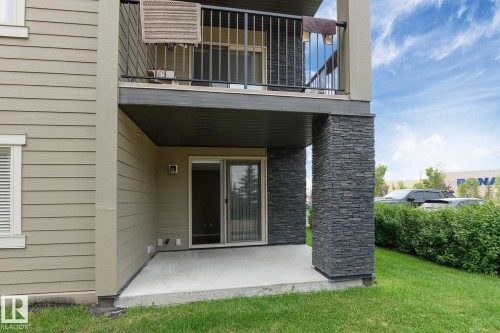 Ground-level patio with sliding glass door access, featuring a stacked stone column accent and a covered overhead balcony - 102 25 Element Dr, St. Albert, AB 