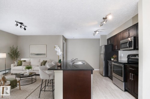 Kitchen featuring dark wood cabinetry, stainless steel appliances, and a central island with a sink and dark countertop - 102 25 Element Dr, St. Albert, AB 
