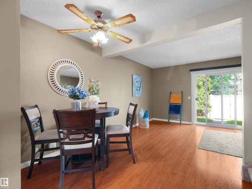 Bright interior space featuring wood-finish flooring, a ceiling fan, and sliding glass patio doors opening to exterior green space - 16 13833 30 Street, Edmonton, AB 
